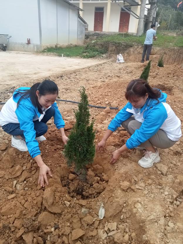 Two women planting a small tree

Description automatically generated